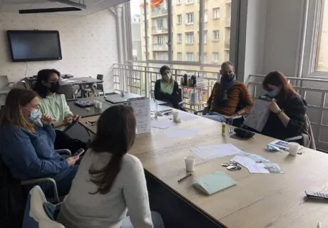 6 personnes qui parlent autour d'une grande table de réunion sur laquelle se trouve des feuilles de papier.