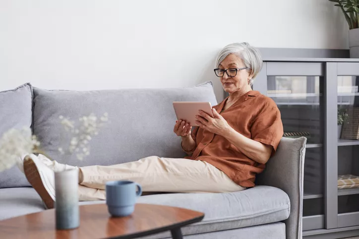 Photo d'une femme âgée utilisant une tablette sur son canapé.