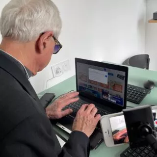 Personne malvoyante testant une interface web sur un ordinateur. Sa navigation est filmée par un téléphone grâce à un trépied.